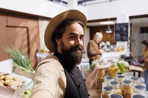 Zero waste shop entrepreneur using selfie camera on mobile phone to promote environmentally responsible vegan products online. Bio supermarket owner making marketing content photo