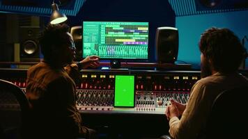 Team of producer and artist use tablet with mockup display in professional studio, mixing and mastering tracks after recording session. Experts working in control room with console. Camera B. video