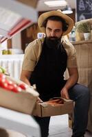 Trader adding crates full of farm grown vegetables from his own garden on zero waste shop shelves. Storekeeper restocking local neighborhood store with chemicals free food items photo