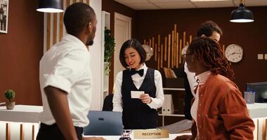 Tourists handing over room access key to friendly asian receptionist at front desk. Happy guests checking out from hotel after nice stay while concierge employee communicates feedback to manager photo