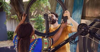 Active sporty interracial couple safely securing front bicycle tire after repair ready for summer cycling. Young caucasian man assisting african american woman with reattaching bike wheel. photo