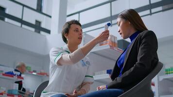 Pharmacist in drugstore using electronic thermometer on asian woman forehead, checking temperature. Patient and healthcare expert during annual examination, monitoring flu symptoms such as fever photo