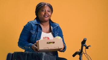 Bicycle is being used by helpful delivery woman to deliver fresh fruits on-demand. Efficient courier service provided by pleasant african american bike messenger with basket of scrumptious vegetables. photo