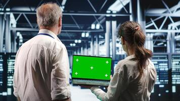 Coworkers in server room expertly managing data while navigating through industrial equipment. Colleagues ensuring flawless cybersecurity defence, optimizing systems using mockup laptop photo