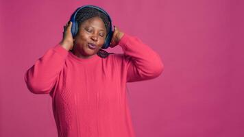 hembra Moda blogger vistiendo inalámbrico auriculares y teniendo divertido con ritmo de favorito música. maravilloso negro mujer en rosado suéter bailando despreocupado disfrutando agradable melodía. foto