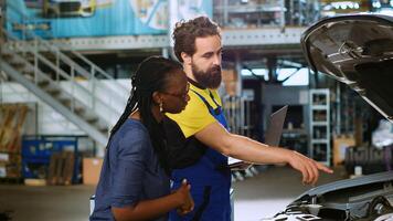 Serviceman in repair shop using laptop to calculate repairments invoice for client after fixing malfunctions found inside car. Expert using device to determine final costs after mending vehicle photo