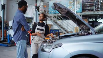 Qualified engineer listens to customer in repair shop, using laptop to write down car modifications needed. Professional in garage workplace with client, listening to her requests for vehicle tuning photo