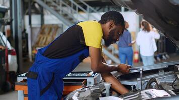 entrenado ingeniero en coche Servicio usos esfuerzo de torsión llave inglesa a apretar tornillos dentro vehículo después fijación componentes adentro. africano americano reparar tienda experto utiliza profesional herramientas a arreglar automóvil foto