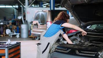 diligente mecánico en garaje utilizando esfuerzo de torsión llave inglesa a apretar tachuelas dentro abrió arriba vehículo después cambiando aceite. auto reparar tienda empleado haciendo mantenimiento en auto, limpiando sobrante lío foto