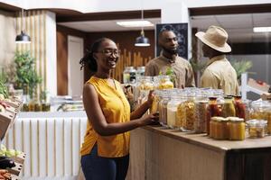 Female customer smiles as she looks at the camera. Sustainable products in reusable containers, wooden shelves. Diverse range of local goods, bulk items. Professional and customer-friendly service. photo