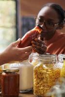 Customer shopping for vegan sustainable food items in a zero waste shop with vendor providing information. Environmentally friendly woman analyzing homemade sauces ideal for healthy eating. photo