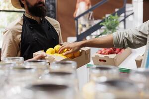 Selective focus on box of fresh lemons carried by salesman wearing a hat and apron in local market. Male customer picking locally grown bio produce from the caucasian vendor. photo