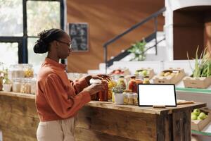 African american female customer browsing in store near a tablet showing isolated chromakey mockup template. Black woman standing next to digital device with a blank white screen. photo