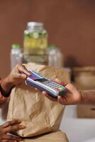 Detailed image of african american female customer paying with a credit card at the checkout counter. Closeup shot of black vendor holding the pos machine for the client to make cashless payment. photo