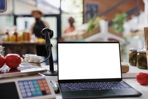 Black laptop with blank white screen placed on a counter next to a measuring weight scale machine in environmentally friendly store. Wireless computer displaying isolated chromakey mockup template. photo