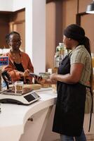 African American female client smiles while using her credit card for cashless payment. The local food market focuses on locally grown organic produce and eco friendly practices. photo