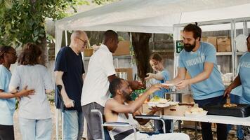 humanitario ayuda equipo Proporcionar asistencia a el minusválido, pobre y Vagabundo gente. caridad trabajadores dando lejos gratis comida a negro hombre en silla de ruedas reunión su necesidades mientras otros Espere en línea. foto