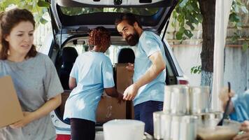 pobre, necesitado y Vagabundo personas son ayudó por caridad trabajadores a un sin ánimo de lucro comida conducir programa. donación cajas son previsto a el Menos afortunado por joven multiétnico voluntarios trípode disparo. foto