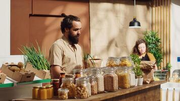 Vegan man in zero waste supermarket adding pantry staples to biodegradable paper bag while shopping. Customer in sustainable local grocery shop eschewing single use plastics policy photo