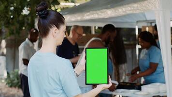 caucásico dama participación inteligente tableta con un chromakey Bosquejo modelo para personalizable caridad mensajes hembra voluntario verticalmente agarra un digital artilugio con aislado verde pantalla mostrar. foto