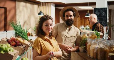 Portrait of happy vegan couple buying pantry staples from zero waste supermarket. Smiling clients shopping for bulk food products in reusable jars from local neighborhood store, zoom in shot photo