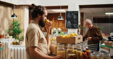 Man in zero waste store shopping for fruits, feeling dopamine rush while smelling them. Client experiencing nostalgic bliss while feeling nice lemons aroma in local shop, zoom out shot photo