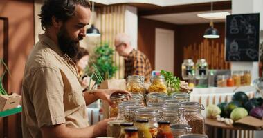 Man in zero waste shop checking products before making purchase decision, making sure they are pesticides free. Green living client verifying pantry staples displayed in local store are organic photo