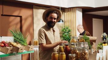 retrato de contento vegano hombre en especialidad cero residuos supermercado utilizando compras cesta a compra abultar artículos en ecológico contenedores cliente en local barrio tienda comprando conservantes gratis comida foto