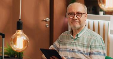 Older man tourist on lounge area sofa, surfing the web on digital tablet. Person holding device to browse internet waiting to see room at five star hotel on vacation, checks online reservation. photo