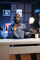 African american entertainer presenting laptop from brand sponsoring video, urging viewers to purchase it. Man does influencer marketing by advertising digital device to audience photo