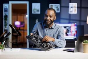 Artist filming DJ mixing tutorial in apartment studio, turning volume knobs and showing examples of sampling. Audio engineer showing sound controller equipment to viewers photo