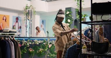 Tracking shot of customer in clothing store during promotional season looking to purchase cheap garments. Client taking advantage of sales in fashion boutique, looking at clothes on racks photo