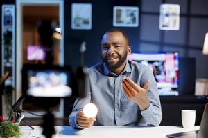 Content creator discussing with fans best ways to enhance home automation, showcasing latest intelligent light bulb to audience. Cheerful tech enthusiast demonstrating Wi-Fi-based IoT technology photo