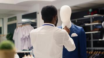 Employee tightening elegant blazer necktie on mannequin in luxurious clothing store. Worker arranging new collection stylish high class attire garments in premium fashion boutique photo