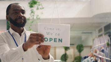 africano americano hombre apertura Moda boutique negocio, comenzando cambio en el Mañana. sonriente detallista torneado cerrado firmar en rápido Moda ropa Tienda dentro abierto uno, cerca arriba Disparo foto