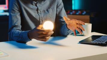 African american content creator in dimly lit living room uses camera to film light bulb review for online streaming platforms. Media star hosts internet show, unboxing smart home technology photo