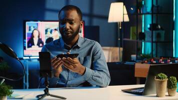 African american technology content creator filming review of newly released smartphone, greeting audience and presenting them feedback about phone specifications, doing endorsement photo