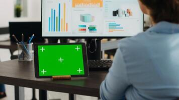 Company employee having tablet on desk with greenscreen display in startup agency office, using blank mockup template and isolated chromakey layout. Woman looking at digital web app on device. photo