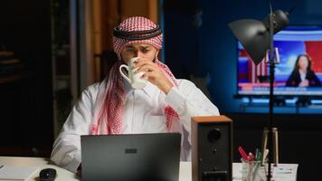 Arab job candidate enjoying beverage while remotely being interviewed by human resources team. Muslim man drinks coffee while getting his credentials checked during online video conference meeting photo