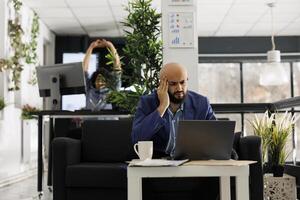 Arab executive manager suffering from migraine while working on laptop in start up business office. Exhausted company financial analyst having headache and touching temples photo