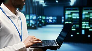 Developer walking through mainframe rows delivering web content to online clients. Programmer in data center using laptop to make sure critical systems are in optimal condition, close up photo