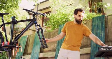 Sports enthusiast man using professional wrench for adjusting bike front fork. Active male cyclist disengaging broken wheel in the yard and using specialized work tool for repairing bicycle. photo