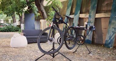 Modern bicycles positioned and secured in backyard in preparation for yearly summer maintenance. Side-view shot of an outside professional toolbox near broken bike on repair-stand. photo