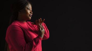 Side-view portrait of female model performing timeout, pause motion on camera. African american woman in black background displaying a t shape stop symbol with her arms, indicating no. photo