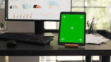 Workstation with greenscreen on tablet in agency coworking space, running isolated chromakey template on mobile device display. Empty office desk showing gadget with blank copyspace layout. photo