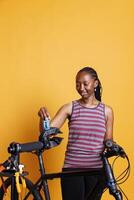 Youthful female cyclist of african american ethnicity inspects broken bicycle components with tools. Black woman expertly and precisely arranging repair stand for bike adjustments and maintenance. photo