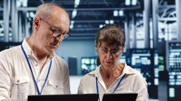 Coworkers looking around high tech data center, using laptop and tablet to crosscheck disaster recovery plan and assess server units in need of replacement, preventing malfunctions photo