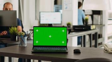 Greenscreen laptop in coworking space placed on empty office desk, open floor plan business workplace with isolated display. Portable computer running blank chromakey layout on software. photo