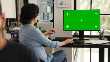 Office employee looks at greenscreen sitting at workstation, checking isolated chromakey display on computer monitor. Woman typing information and examining blank mockup desktop. photo