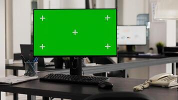 Empty desk with computer shows greenscreen on monitor, running blank mockup copyspace in business office. Workstation in open floor plan office with pc and isolated chromakey template. photo